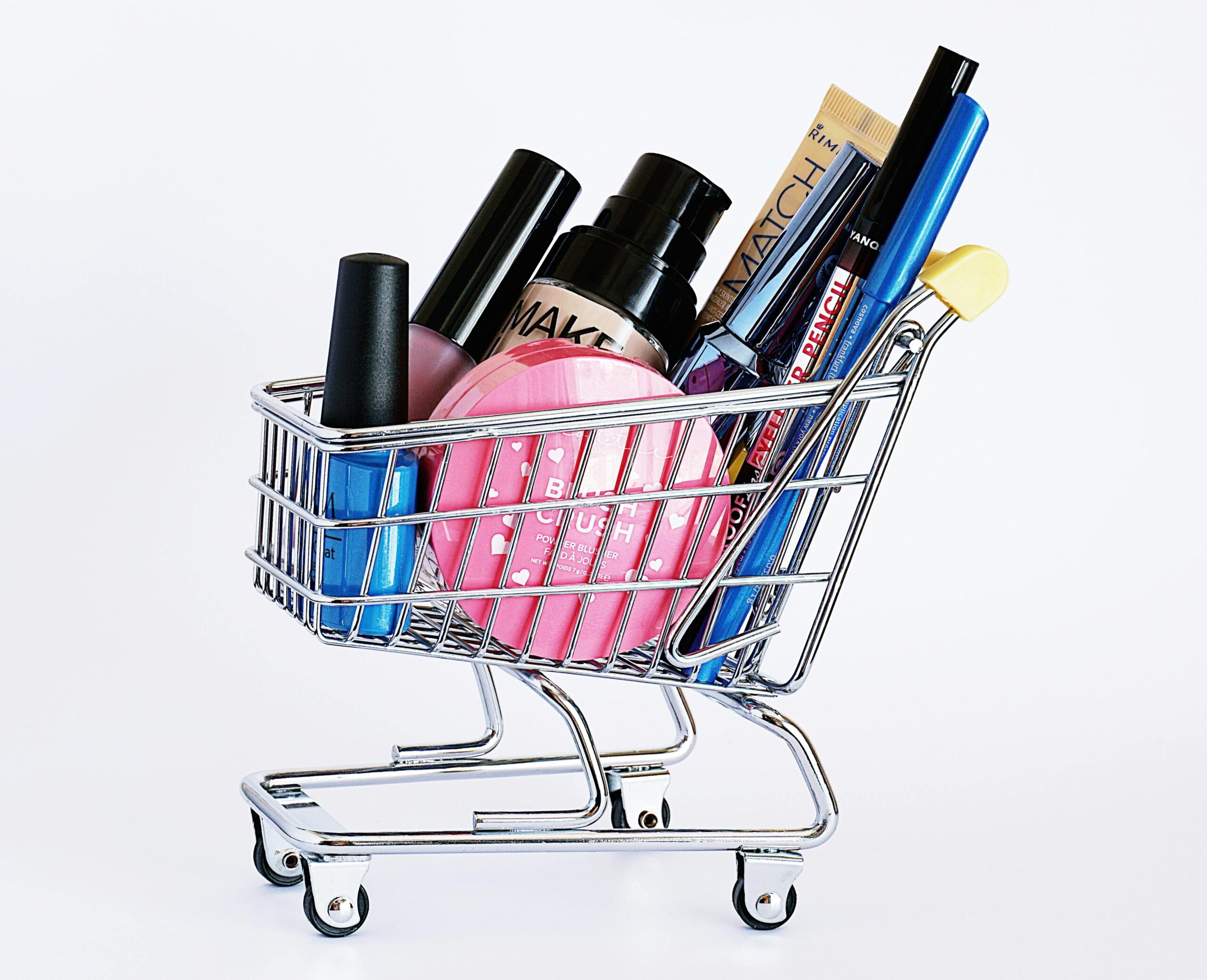 About Miniature shopping cart filled with a variety of cosmetics on a white background.