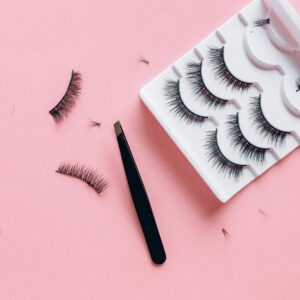 Home Stylish arrangement of false eyelashes and tweezers on a pink background, perfect for beauty themes.