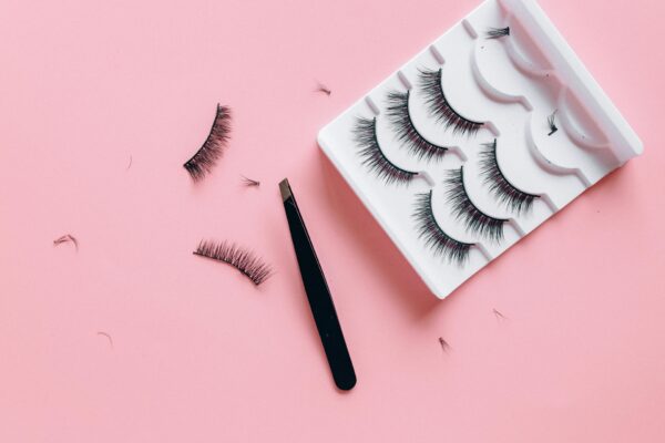 Stylish arrangement of false eyelashes and tweezers on a pink background, perfect for beauty themes.